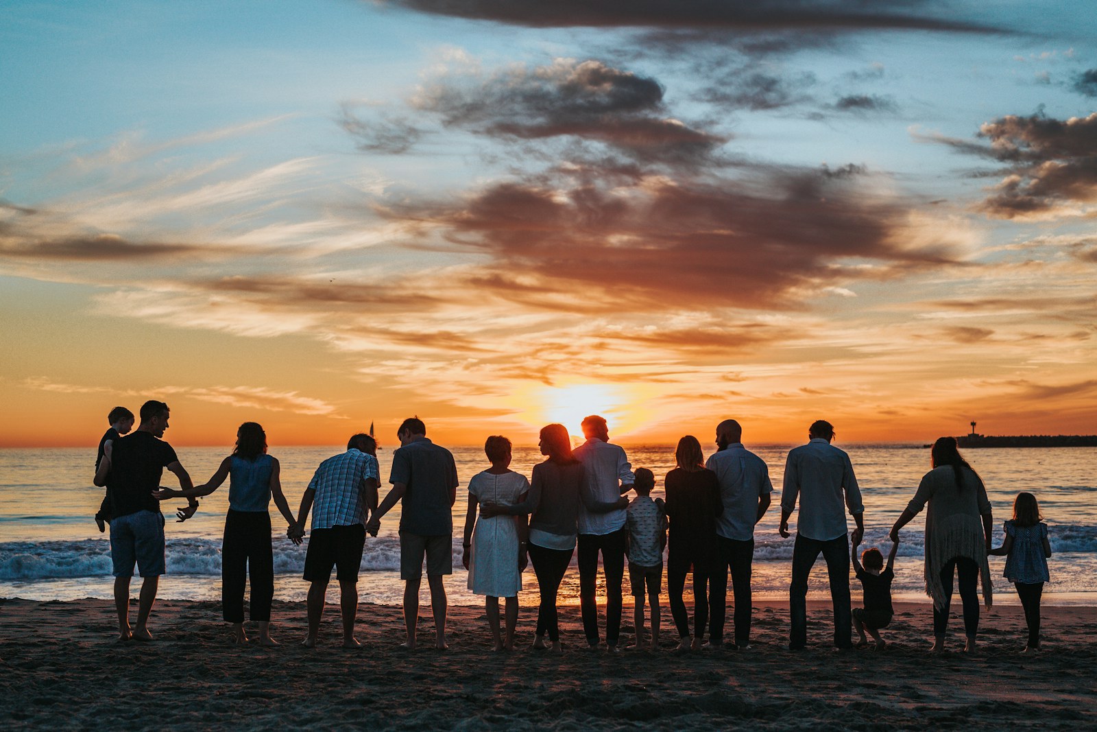 Multigenerational family standing hand in hand on a beach at sunset